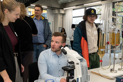 Besucher und Ronja Weidemann vor dem Mikroskop am Stand in der BCI-Galerie